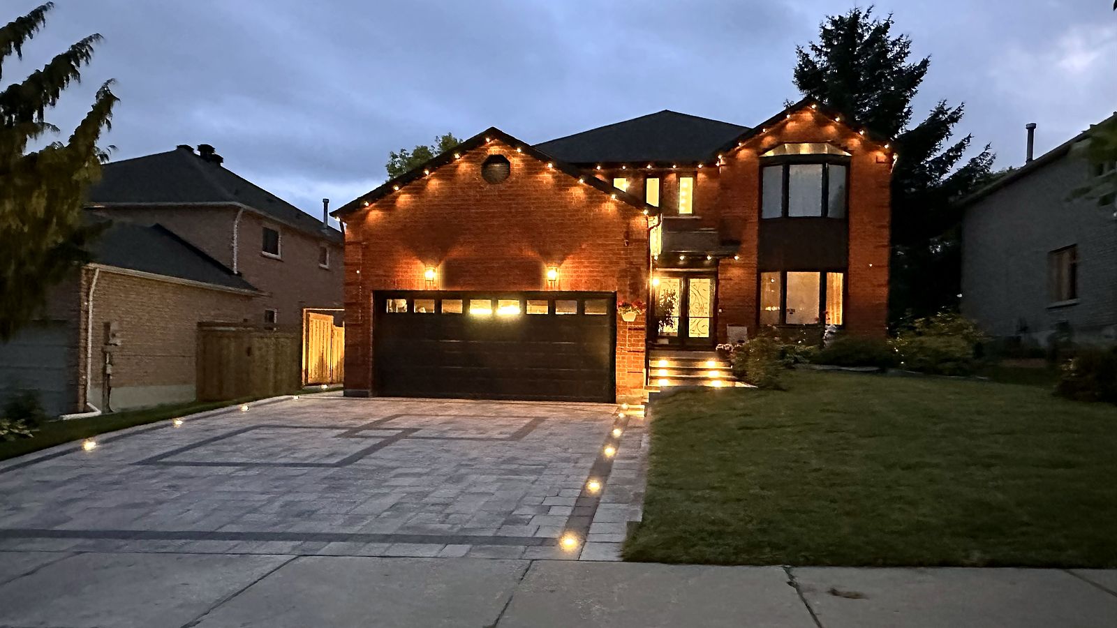 A red-brick Newmarket home at dusk, lit up, with its interlock driveway