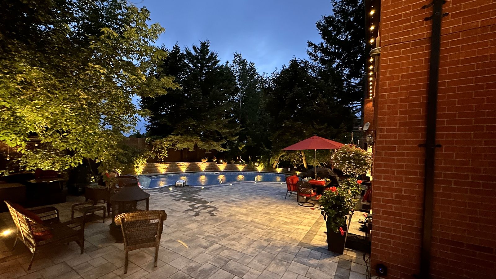 A backyard pool and patio at dusk, lit along the fence and the pool edge