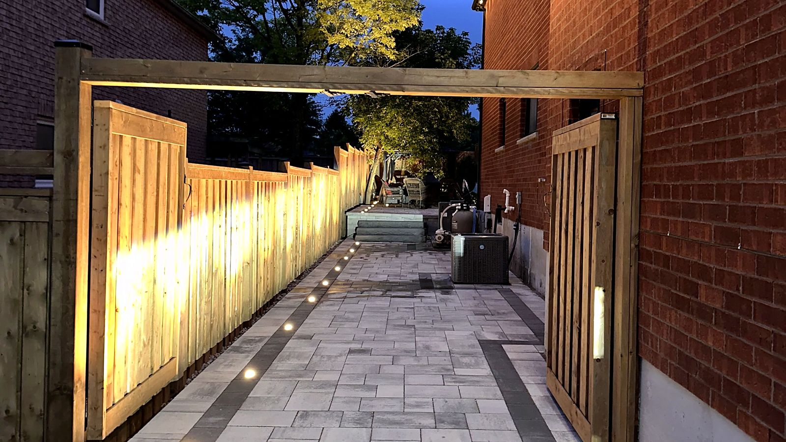 A lit side path and cedar fence leading to the backyard at dusk